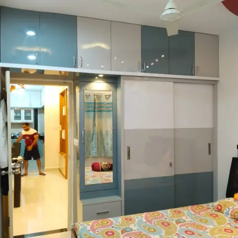 Lived-in bedroom shot past a paisley bedspread towards a powder-blue and grey gloss sliding wardrobe with a loft run