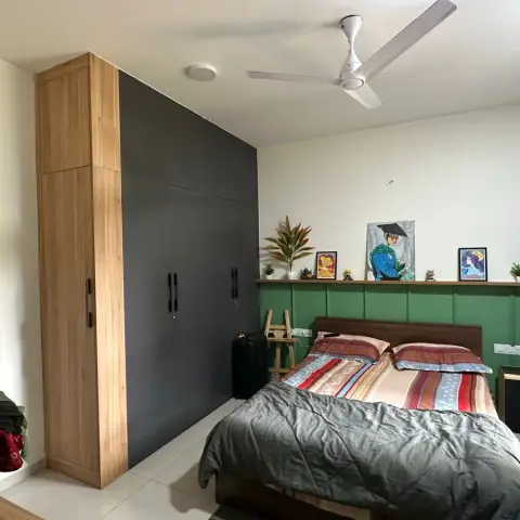 Lived-in bedroom where a forest-green panelled dado topped with a slim oak ledge runs behind the bed, holding framed portraits