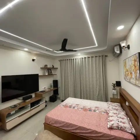 Lived-in bedroom with a curved teak-and-cream wall-hung TV unit flanked by floorstanding speakers