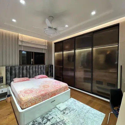 Lived-in bedroom with a grey channel-tufted headboard wall running behind the bed into two bedside units, a full-width sliding wardrobe in bronze-tinted glass