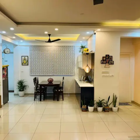 Lived-in flat photographed from the hall toward a four-seater dark wood dining table under a stepped cove-lit ceiling with a black fan