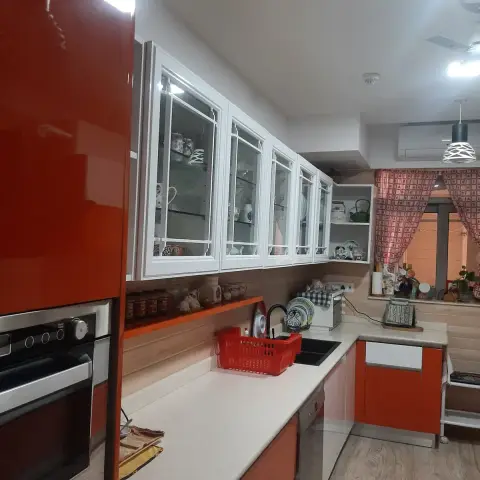 Lived-in L-shaped kitchen with high-gloss red base units and a red tall unit housing a built-in oven and microwave
