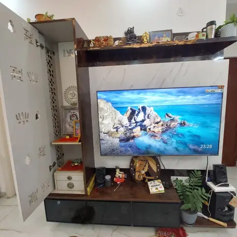 Lived-in living room TV wall in marble-print laminate with a dark wood ledge of brass idols and family photos above it