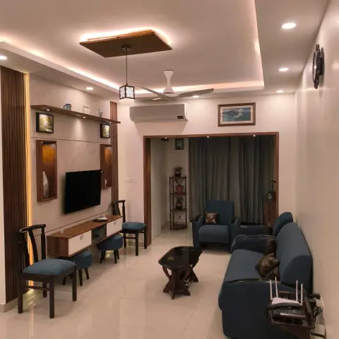 Lived-in living room with a beige marble-effect TV panel carrying walnut-lined lit niches and a floating console, teal-blue sofas along the opposite wall