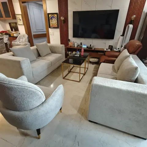Lived-in living room with three grey chenille sofas and a curved bouclé armchair around brass-legged black-glass nesting tables