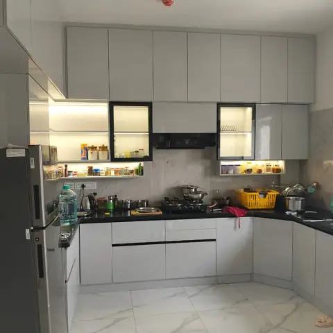 Lived-in U-shaped kitchen in matt light-grey handleless shutters with black granite counters, two black-framed glass cabinets holding plate racks