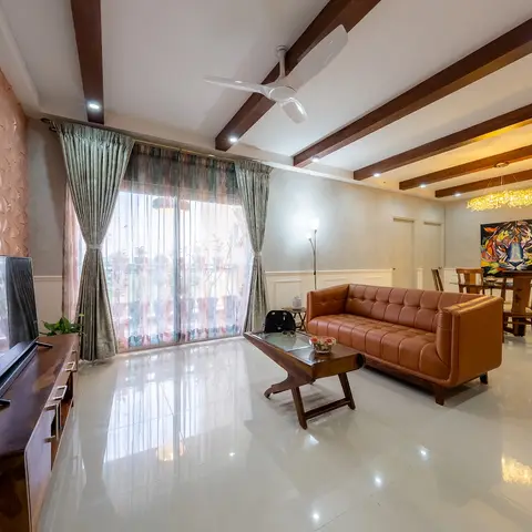 Living and dining space with a tan leather tufted sofa and wood coffee table in the foreground, layered sheer curtains at the balcony door