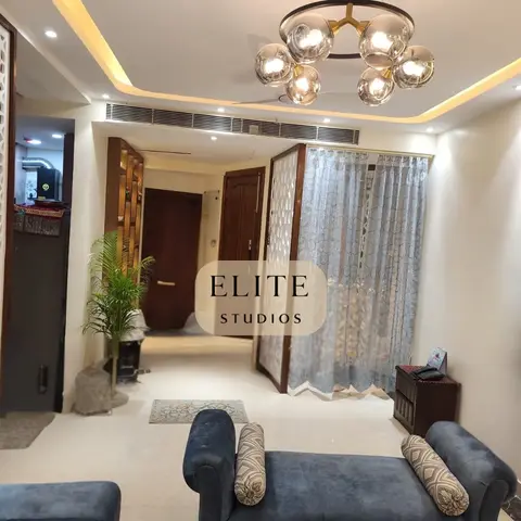 Living area entrance with a carved white jaali partition screen, a cove-lit ceiling with a multi-globe chandelier, and a blue tufted bench seat.