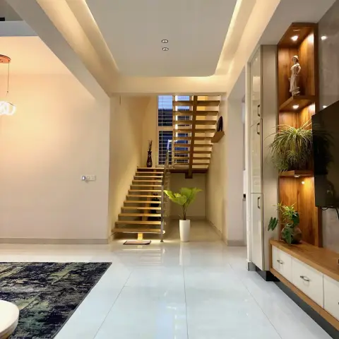 Living area with a white-and-teak TV unit whose lit open niches hold trailing plants and a figurine, a dark abstract rug at the left