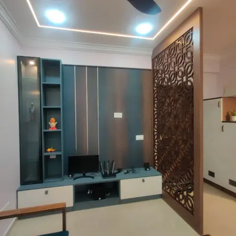 Living corner where a denim-blue TV unit with metal inlay strips and a glazed display column stands beside a full-height CNC walnut jaali that screens the