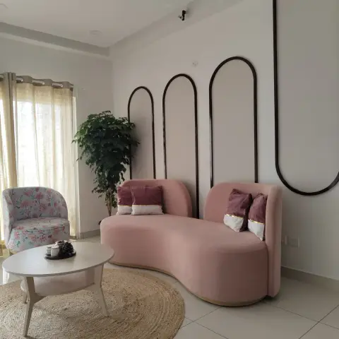Living corner with a kidney-shaped blush velvet sofa on a brass base, set against three slim black arch mouldings on a white wall