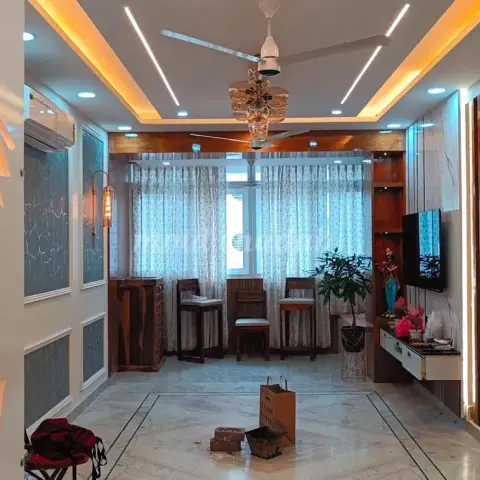 Living-cum-foyer space with a backlit floral jaali cutout panel, fluted wood pillars, cove-lit ceiling