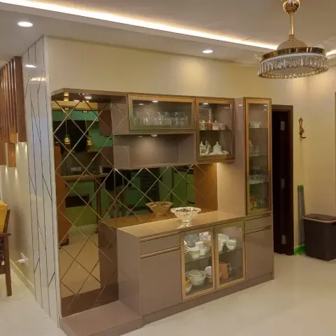 Living-dining area with a mirrored diamond-pattern crockery display unit, a crystal chandelier ceiling fan, and a wood-slat partition beside a wooden armchair