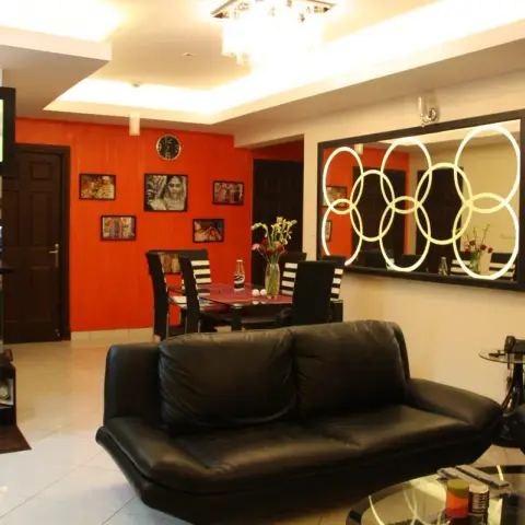 Living-dining combo with a black leather sofa set facing a ring-motif backlit mirror on a cream wall
