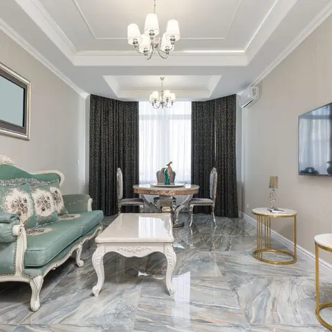 Living-dining room with a mint-green tufted French-style sofa, dramatic grey-veined marble flooring and a gilded peacock statue centerpiece on the dining table.