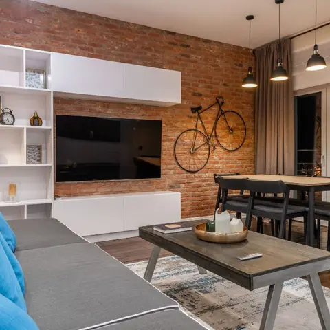 Living-dining room with an exposed brick TV wall, a wall-mounted bicycle ornament and black pendant lights over the dining table