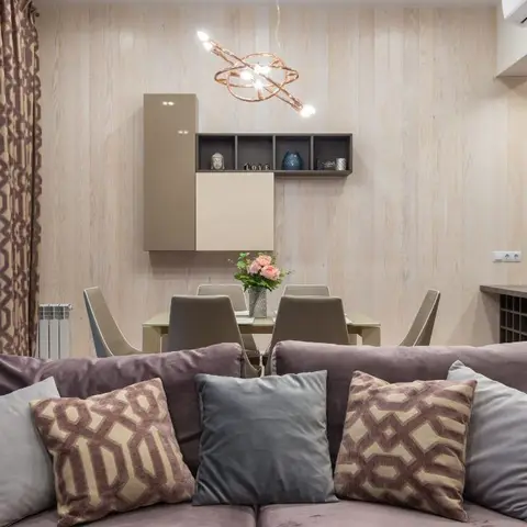 Living-dining space with a light wood-panelled wall, a sculptural copper ring pendant over the dining table