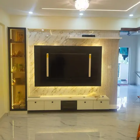 Living hall TV wall on handover day, protective film still taped to the screen: a white-and-gold marble-look clad panel backlit around a black TV recess