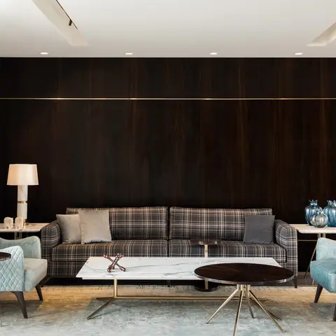 Living lounge with a dark rosewood panelled feature wall, plaid sofa flanked by quilted teal velvet armchairs, and marble-and-brass coffee tables.