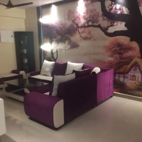 Living room accented by a large tree-and-cottage mural wallpaper behind a purple-and-white sofa set with a glass-top coffee table.