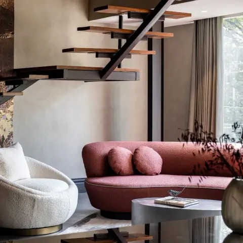 Living room beneath a floating black-steel staircase with wood treads, featuring a curved terracotta boucle sofa, a round cream boucle armchair