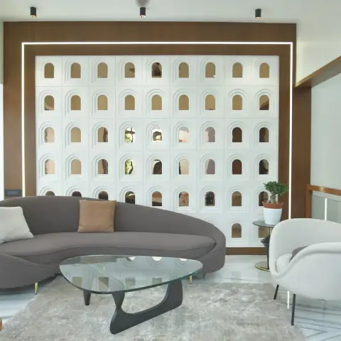 Living room built around a five-by-nine grid of white arched jaali openings backed with mirror, framed in walnut veneer with a slim LED reveal