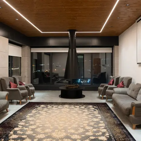 Living room centered on a black conical suspended fireplace beneath a wood-clad ceiling with linear cove lighting