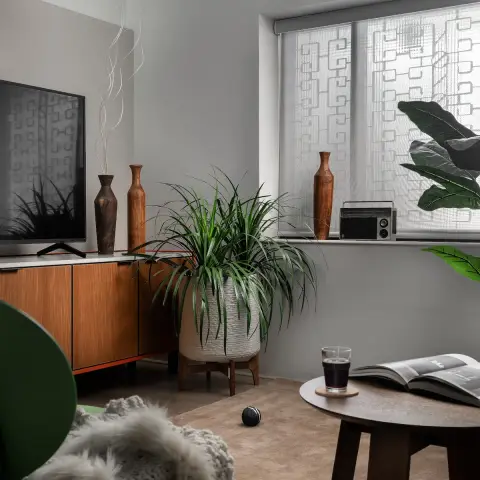 Living-room corner where a teak sideboard on an orange plinth carries the TV beside turned wooden vases and a vintage transistor radio