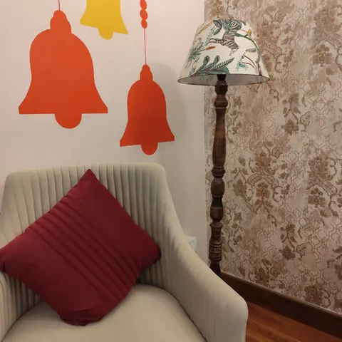 Living room corner with a beige channel-tufted armchair and a maroon cushion beside a wood floor lamp with a printed animal-motif shade