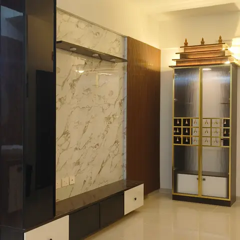 Living room corner with a black-and-marble TV feature wall beside a freestanding gold-trimmed pooja unit that has fluted glass doors and a tiered temple-style