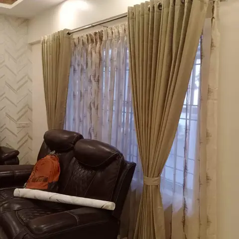 Living room corner with a black leather reclining sofa in front of layered gold curtains over sheer inner drapes, chevron-pattern wallpaper on the side wall.