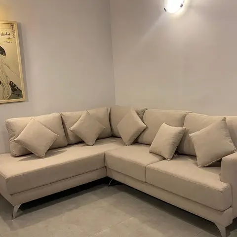 Living room corner with a cream L-shaped sectional sofa piled with matching cushions beneath a framed Japanese woodblock-style print.