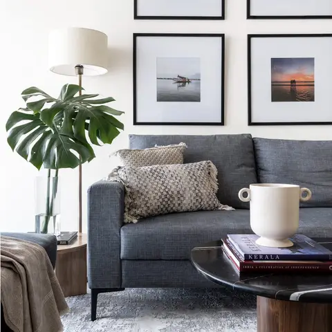 Living room corner with a grey linen sofa styled with textured cushions beneath a four-frame gallery wall of travel photographs
