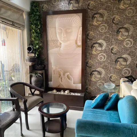 Living room corner with a large carved Buddha relief panel on a patterned wallpaper wall, a teal velvet sofa
