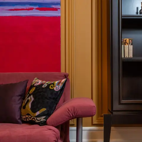 Living room corner with a maroon velvet sofa piled with embroidered cushions beneath a large abstract red-and-blue painting