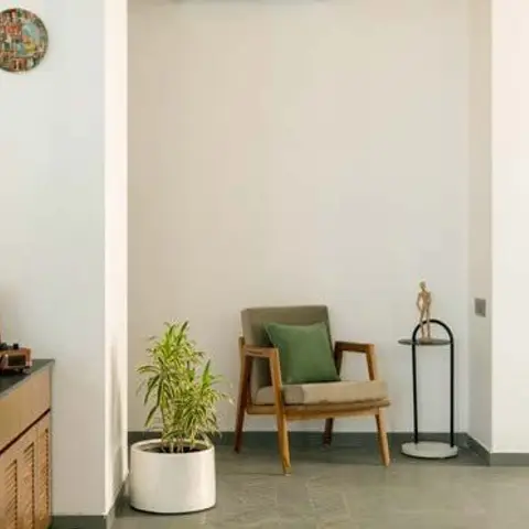 Living room corner with a mid-century wood-frame armchair and green cushion, a wood sideboard with a vintage record player, and a potted palm.
