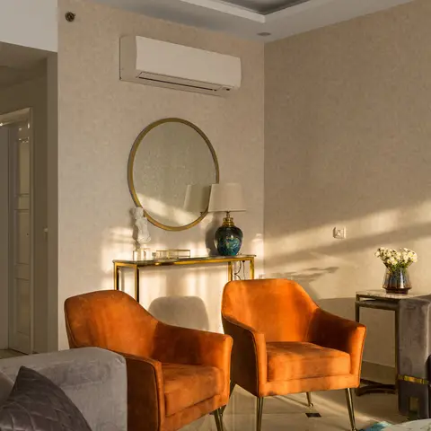 Living room corner with a pair of burnt-orange velvet armchairs, a round brass-framed mirror over a glass console table