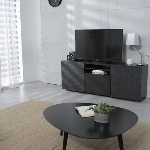 Living room corner with a raw-concrete-panel accent wall behind a black textured TV console, a black oval coffee table on a jute rug