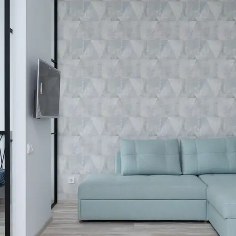 Living room corner with a seafoam-mint L-shaped sectional sofa against a grey geometric triangle-pattern wallpaper wall, a wall-mounted TV