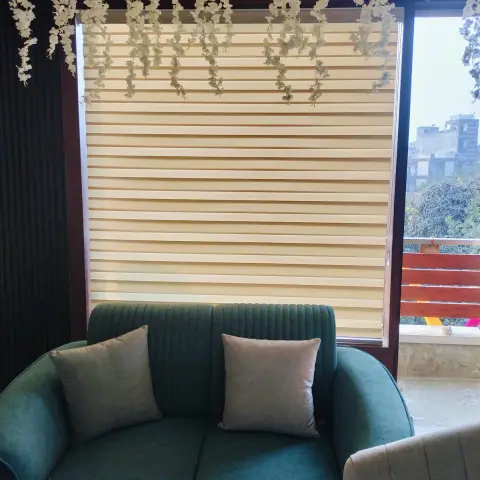 Living room corner with a teal channel-tufted sofa and grey cushions in front of a zebra-blind window
