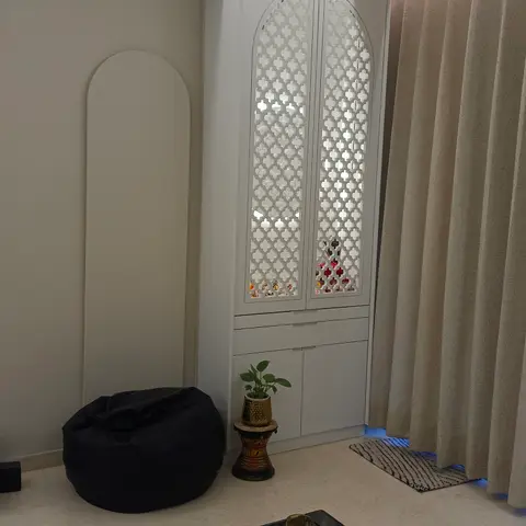 Living room corner with a white jaali-pattern pooja cabinet in an arched wardrobe, a black bean bag, and a styled black coffee table with candles