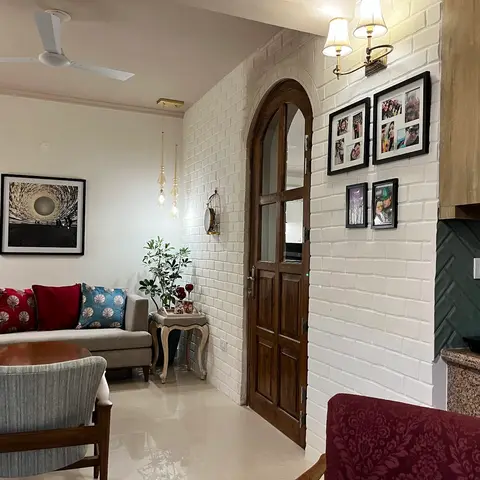 Living room corner with a white-washed brick archway framing a wooden arched door, a gallery wall of photo frames