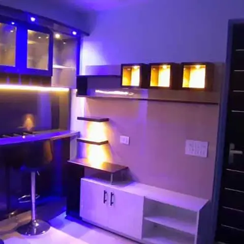Living room corner with an LED-lit home bar counter and glass cabinet, plus a floating TV wall unit with lit display cubes.