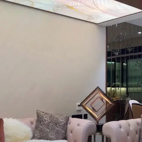 Living room corner with blush pink tufted chesterfield sofas, a backlit onyx ceiling panel, and a mirrored fluted partition leading to the dining area beyond.