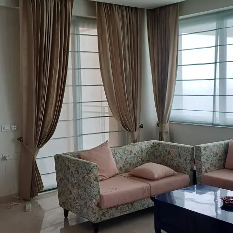 Living room corner with floor-to-ceiling mocha curtains over sheer roman blinds, a floral chintz sofa with blush cushions, and a navy lacquered coffee table.
