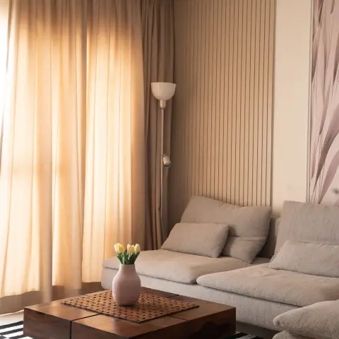 Living room corner with fluted wall panelling, a beige upholstered sectional sofa, a striped rug, and a solid-wood block coffee table.
