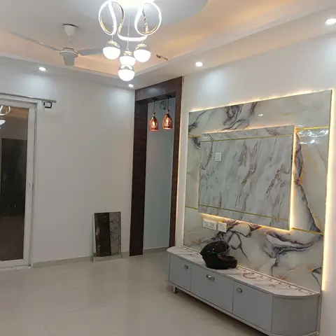 Living room entry wall with a backlit gold-veined marble panel above a grey console, ring pendant chandelier and cove-lit ceiling.