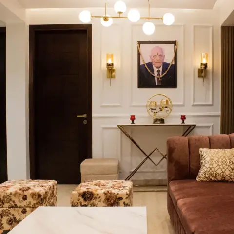 Living room entry with white wainscot panel moulding, brass wall sconces flanking a framed portrait, a gold X-base console table