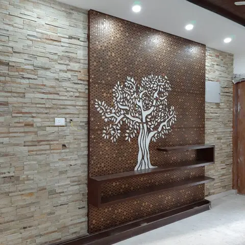 Living room feature wall combining stacked natural-stone cladding with a backlit CNC-cut tree-motif panel over a floating dark-wood shelf