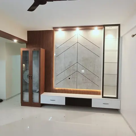 Living room feature wall with a chevron-textured stone panel, fluted walnut surround, floating white TV console, and a glass display cabinet.